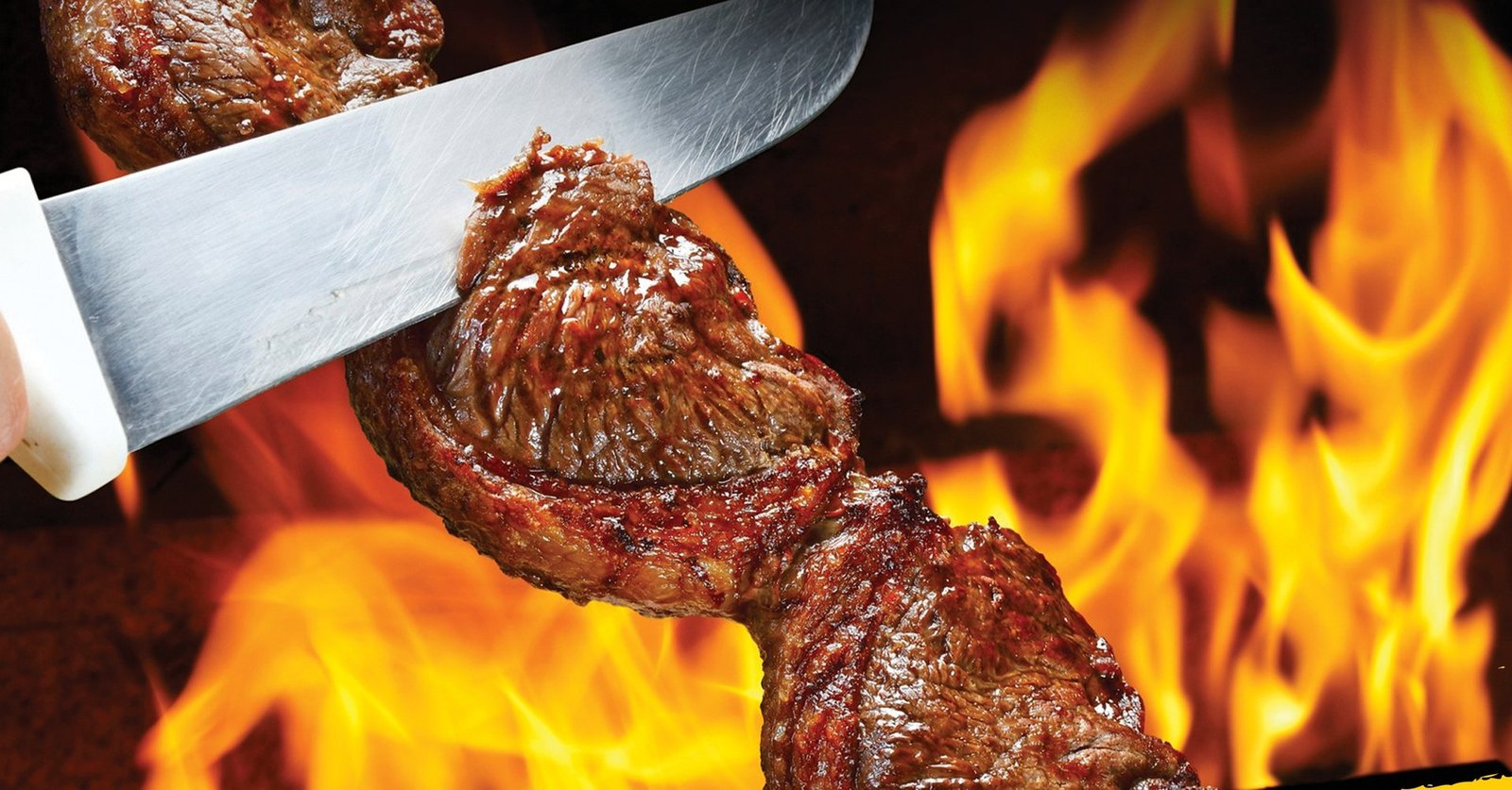 Picanha na brasa sendo fatiada com faca, fogo ao fundo — Churrascaria Sal da Terra